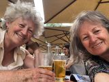 Two woman sitting outside in the sun enjoying a drink and smiling